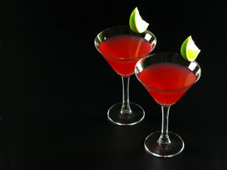 Two bright red Bacardi alcoholic cocktails made of white rum, lime juice and grenadine, in conical cocktail glasses, decorated with lime slices, on a dark background