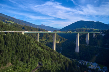 Aerial view of a road bridge in the Alps surrounded by meadows, forests and mountains. Flying on drone.