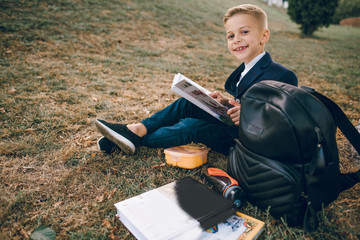 schoolboy sitting on the lawn near the school and reading a book. Back to school.