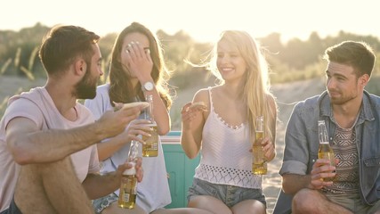 Group of young cheerful friends drinking beer and eating pizza while talking together at the beach