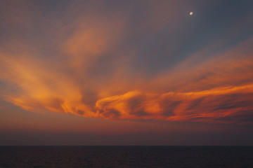 Moon rising over the sea and awesome orange-colored clouds after sunset