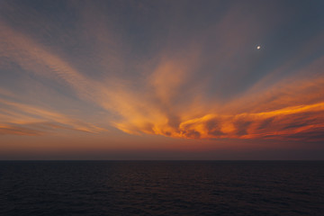 Moon rising over the sea and dreamy orange-colored clouds after sunset
