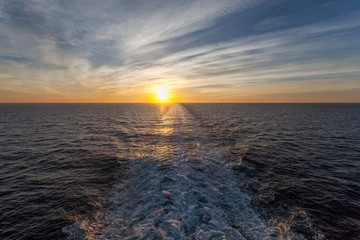 Sun about to set and wake left on the sea by a cruise ship
