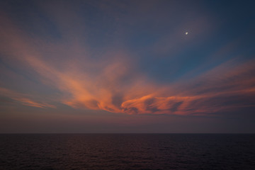 Moon rising over the sea and orange-colored clouds after sunset