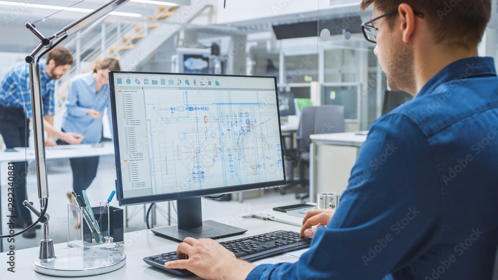 Poster Over the Shoulder Shot of Engineer Working with CAD Software on Desktop Computer, Screen Shows Technical Drafts and Drawings. In the Background Engineering Facility Specialising on Industrial Design