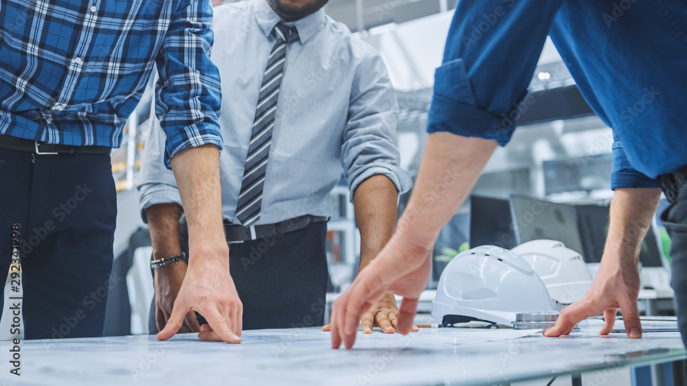 Poster In the Industrial Engineering Facility: Diverse Group of Engineers and Technicians on a Meeting Gather Around Table Unravel Sheets of Engine Design Technical Drafts, Have Discussion, Analyse Drawings