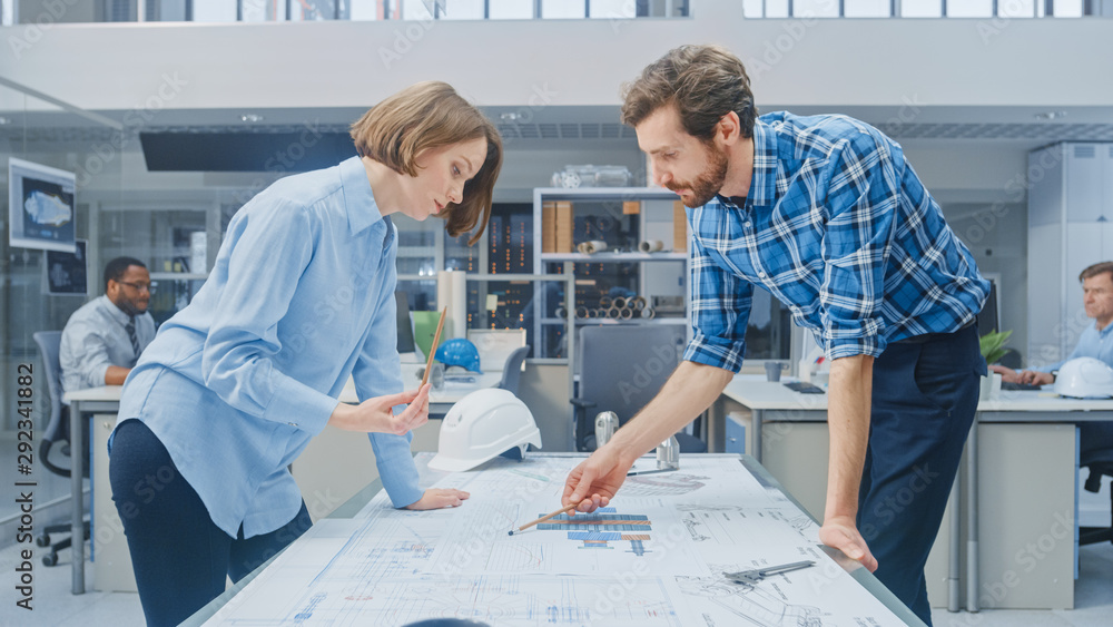 Aufkleber in the industrial engineering facility: young female designer works with chief industrial engineer, 