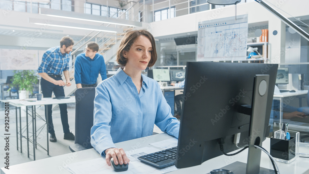 Poster In the Industrial Engineering Facility: Portrait of the Smart and Beautiful Female Engineer Working on Desktop Computer. In the Background Specialists and Technicians Working with Drafts and Drawings