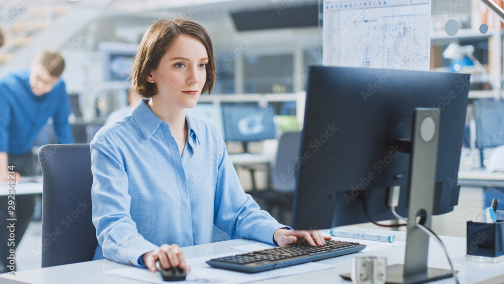 Poster In the Industrial Engineering Facility: Portrait of the Smart and Beautiful Female Engineer Working on Desktop Computer. In the Background Specialists and Technicians Working with Drafts and Drawings
