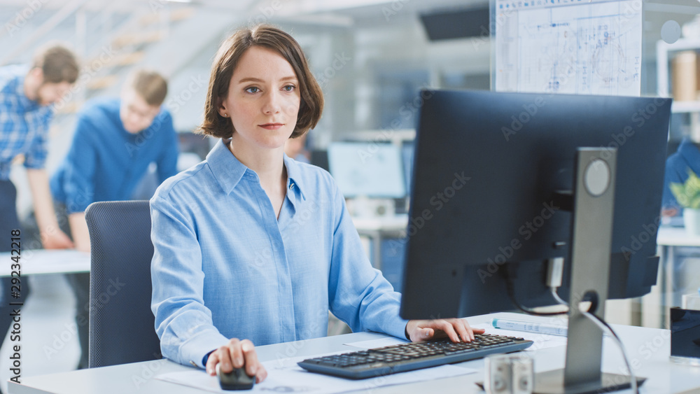 Poster In the Industrial Engineering Facility: Portrait of the Smart and Beautiful Female Engineer Working on Desktop Computer. In the Background Specialists and Technicians Working with Drafts and Drawings