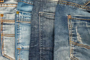 textured background of a variety of denim pants in various shades of blue stacked rows of back pockets up