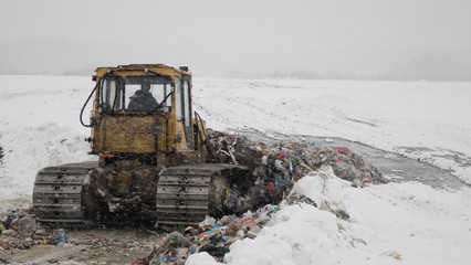 Garbage dump in the snow. Bulldozer rakes a bunch of garbage.