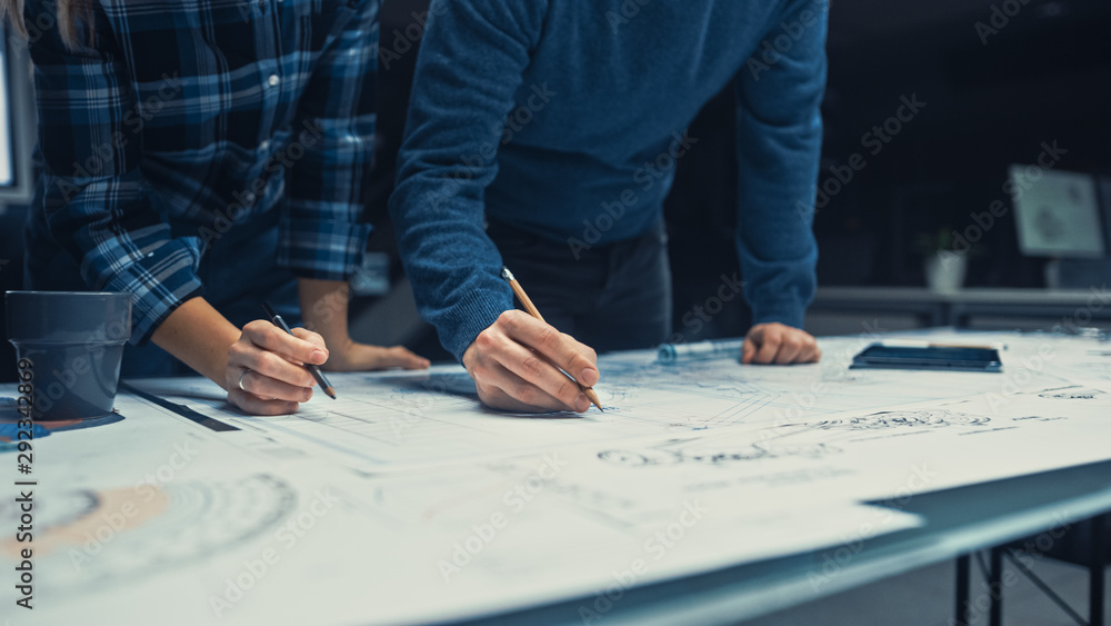 Wall mural close-up shot with focus on hands of male and female engineers work on a blueprints using pencils on