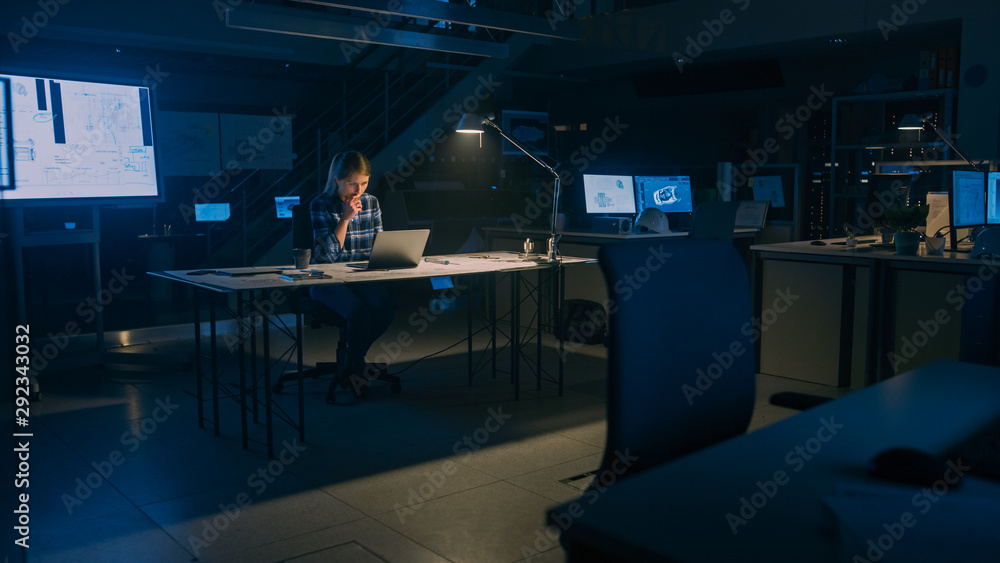 Poster beautiful female engineer sitting at her desk works on a laptop computer. blueprints lying on a tabl