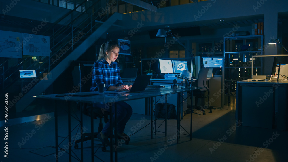 Poster beautiful female engineer sitting at her desk works on a laptop computer. blueprints lying on a tabl