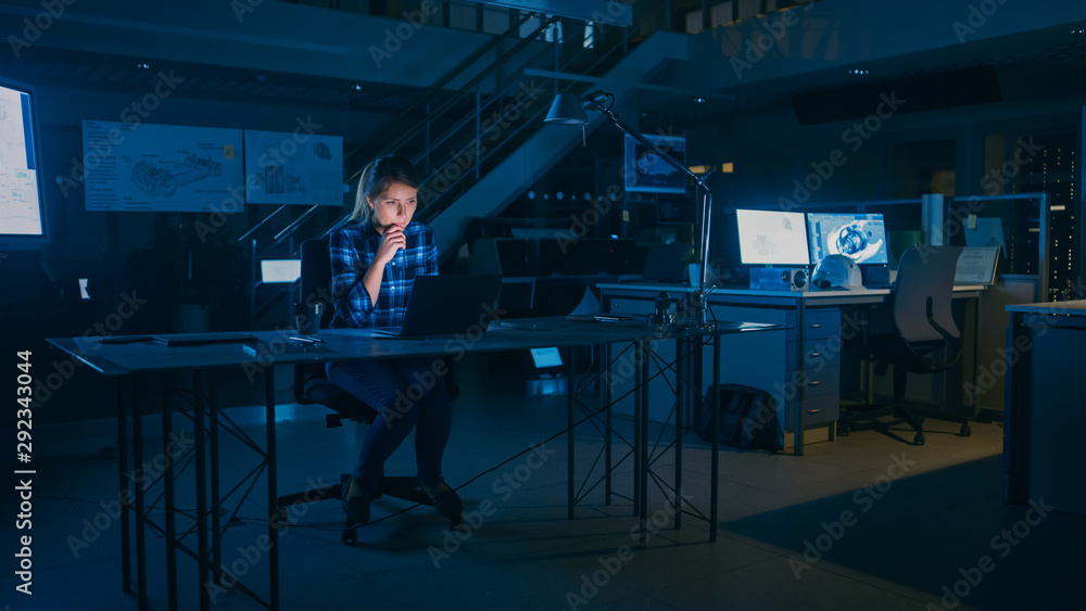 Poster beautiful female engineer sitting at her desk works on a laptop computer. blueprints lying on a tabl