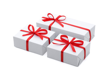 Side view of a geometric composition of three white gift boxes of different sizes tied with a bright red satin ribbon with bows isolated on a white background