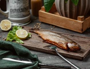 Dried smoked fish served with lemon slices on wooden board