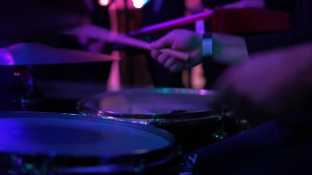 Drummer perform modern music at a party. Man in black perform jazz and soul songs at nightclub. Musician play drum kit with drumsticks in a crowd under muffled lighting, close-up. Relaxing atmosphere.