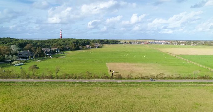 Young Couple Riding A Tandem Bike on the Dutch Island Ameland, The Netherlands. Also in shot: with Red and White Striped Lighthouse, houses, trees, fields, horses. 4K Drone Footage.