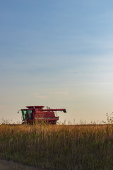 Fototapeta premium Older Red Combine in Field as Sun Sets