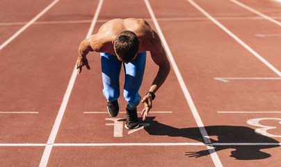 Sprinter man preparing for running on racetrack at stadium. Sportsman, male runner sprinting during training session for competition. People, sport and healthy lifestyle