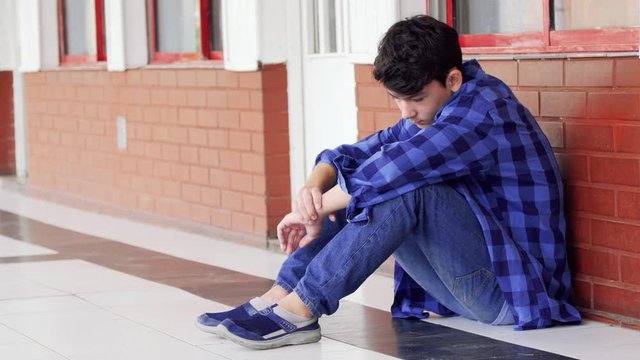 Caucasian boy bullied at school, seated on school hallway. Slow motion