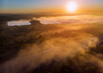 Fantastic foggy lake with sunlight sun beams through tree dramatic colorful scenery.
