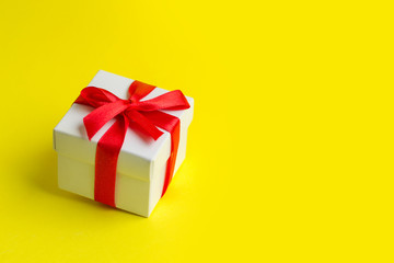 White box with a red ribbon on a yellow background, copy space. Greeting card concept. Gift concept