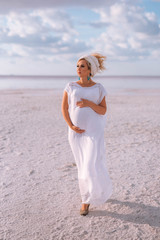 Pregnant woman in a turban and a white dress on a background of blue sky and clouds.