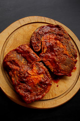 raw meat, beef steaks marinated in a red marinade, lie on a wooden round board, cooking concept, close-up