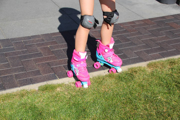 little girl learns riding pink four-wheeled roller skates on the grass, knee pads, legs, close-up