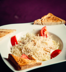 A close up of plate with roasted chichken with grated parmesan cheese and fresh tomatos