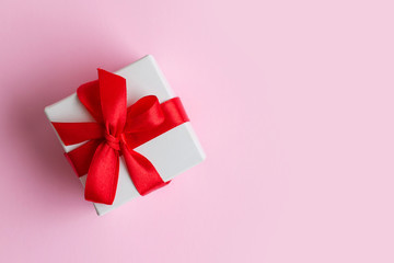 White box with a red ribbon on a light pink background, copy space. Greeting card concept. Gift concept