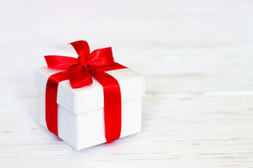 White gift box with a red ribbon on a white wooden background, copy space. Greeting card concept. Gift concept