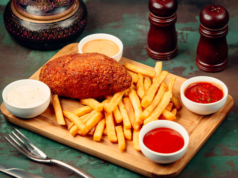 Crispy chicken fillet served on wooden plate with fries and four souces