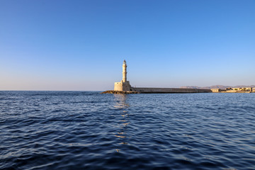 Lighthouse in Chania on a sunny day with blue sky and reflection on water.