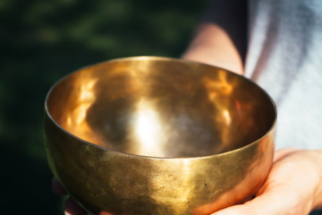 Bronze singing bowl in female palms in the sunlight. A bowl for music, meditation and gaining balance in women's hands.