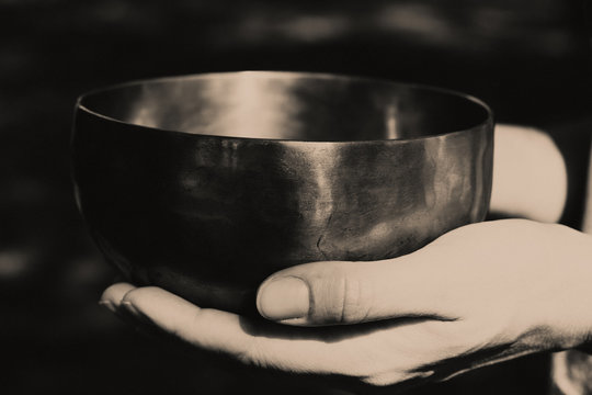 Black and white photo of a bronze singing bowl in female palms. Bowl for meditation and sound balance of concentration in female hands.