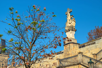 Tree without leaves and a statue with a cross in Prague in autumn