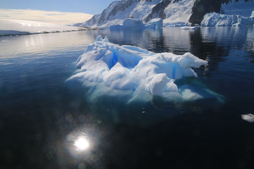 wystający ponad taflę wody wierzchołek góry lodowej przy wybrzeżu antarktydy w słoneczny dzień - obrazy, fototapety, plakaty