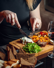 Woman cutting beef steak with melted cheddar cheese and creamy sauce