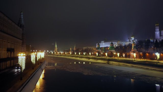 Moscow river is partially covered with ice. Embankment in front of the Kremlin wall. Ancient towers and a famous church. Christmas decorations. Heavy traffic. Winter. Night time. Panorama view. 4K