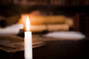 A lit candle against the background of blurred scrolls, books and bird feathers