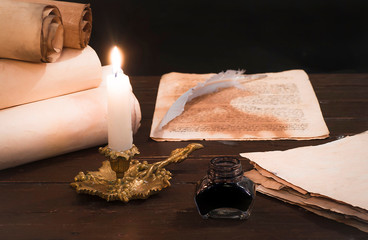 A lit candle on the background of blurred scrolls and bird feathers