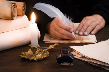 A lit candle against the background of blurred scrolls, writer's hand, books and bird's feather