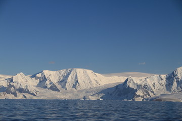 skaliste i ośnieżone wybrzeże antarktydy w słoneczny dzień - obrazy, fototapety, plakaty