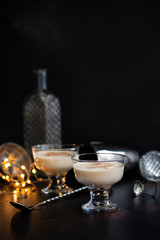 Eggnog traditional Christmas alcoholic drink with cinnamon and nutmeg in two glasses on a dark table with bar tools and Christmas decorations. Winter holidays mood. Dark background. Copyspace