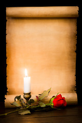 A scroll of parchment, a red rose and a lit candle