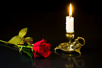 Red rose and candle in a candlestick on a black background